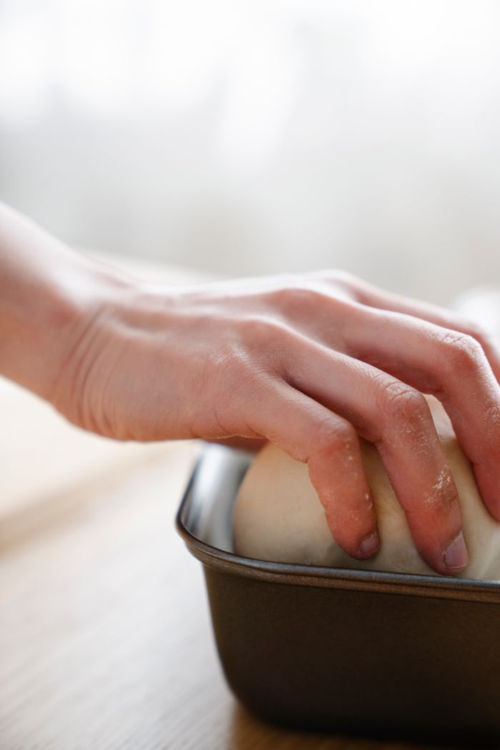 A hand gently kneading dough in a baking pan, showcasing hands-on baking preparation.