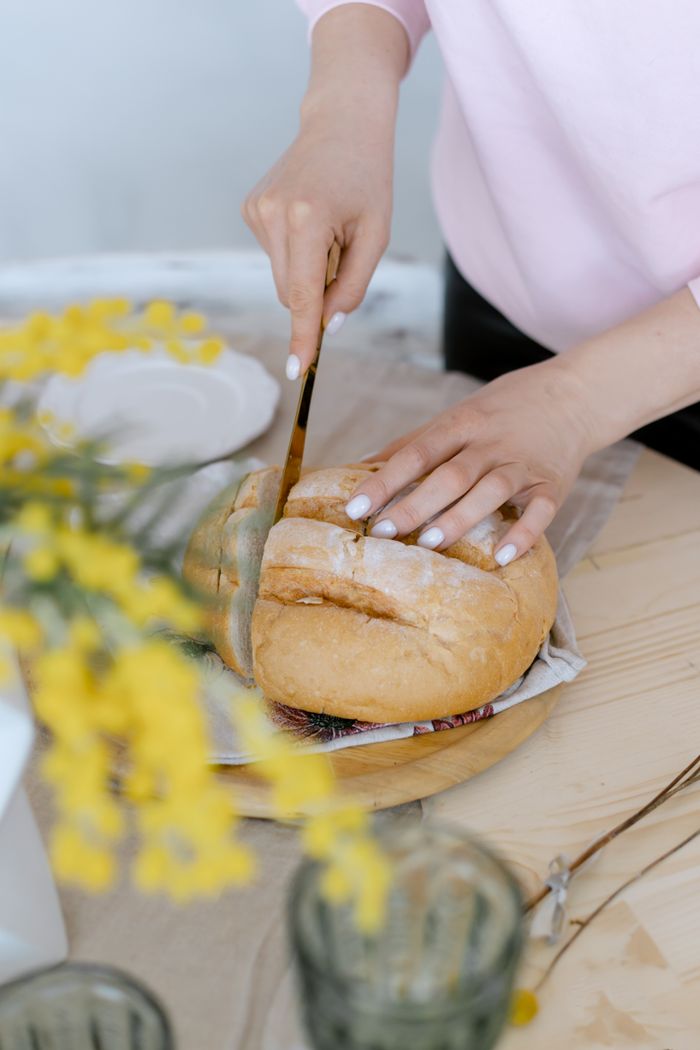 Hands slicing fresh bread on a rustic table with yellow flowers nearby, creating a cozy atmosphere.